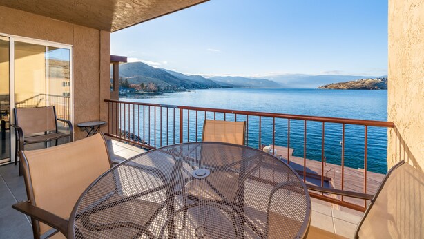 Ein Balkon mit Tisch und Stühlen mit Blick auf einen See und Berge.