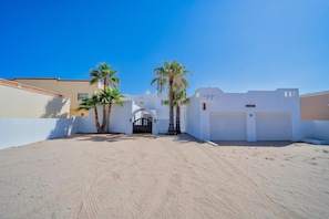 A gated entrance with a clear sky, palm trees, and a white building with a garage.
