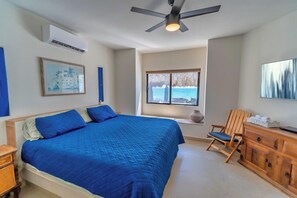 A bedroom with a large bed, a ceiling fan, a window with a view of the sea, a wooden chair, and a desk with a vase. - ALL 4 Master Bedrooms Are Beachfront with King Beds, Remodeled in 2021 (Puerto Penasco)