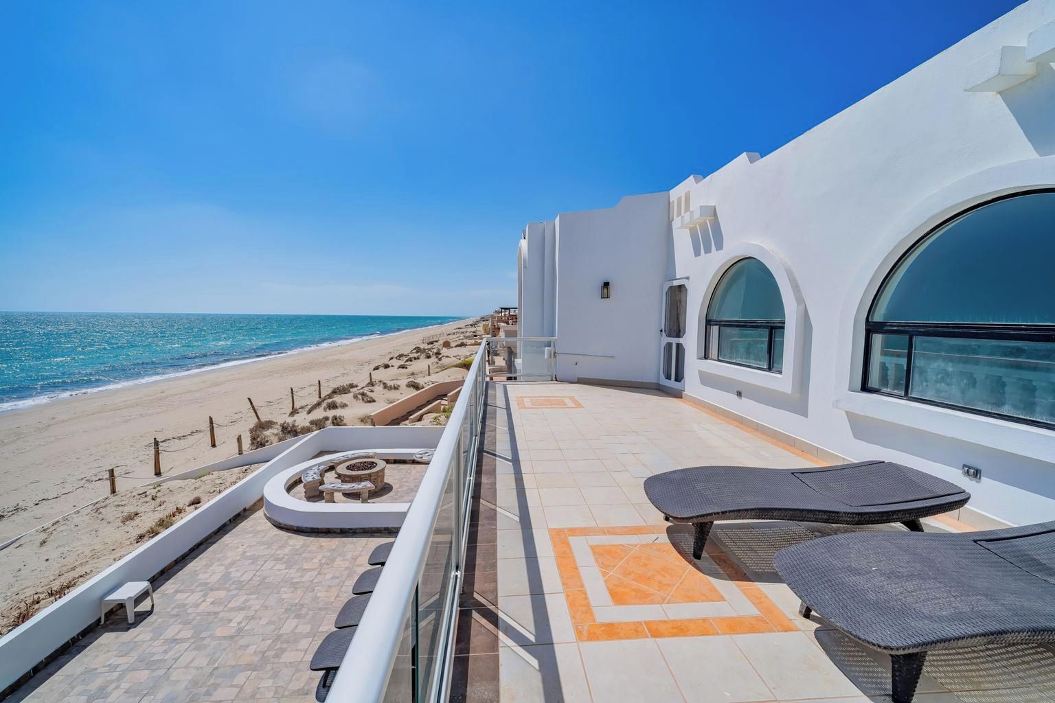 A balcony with a view of the beach, a circular seating area, and a large window overlooking the ocean.