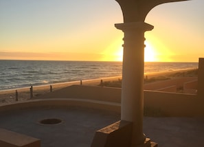 Une vue sur le coucher de soleil depuis un balcon donnant sur une plage, avec une colonne au premier plan.