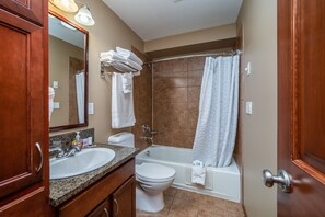 Un baño con lavamanos, inodoro y bañera. Hay toallas y una cortina de ducha.