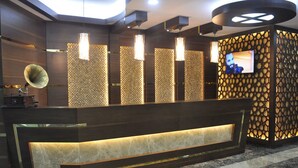 A reception area with a dark wooden reception desk, a patterned wall, and a television screen. - Alemdar Otel (Erzincan)
