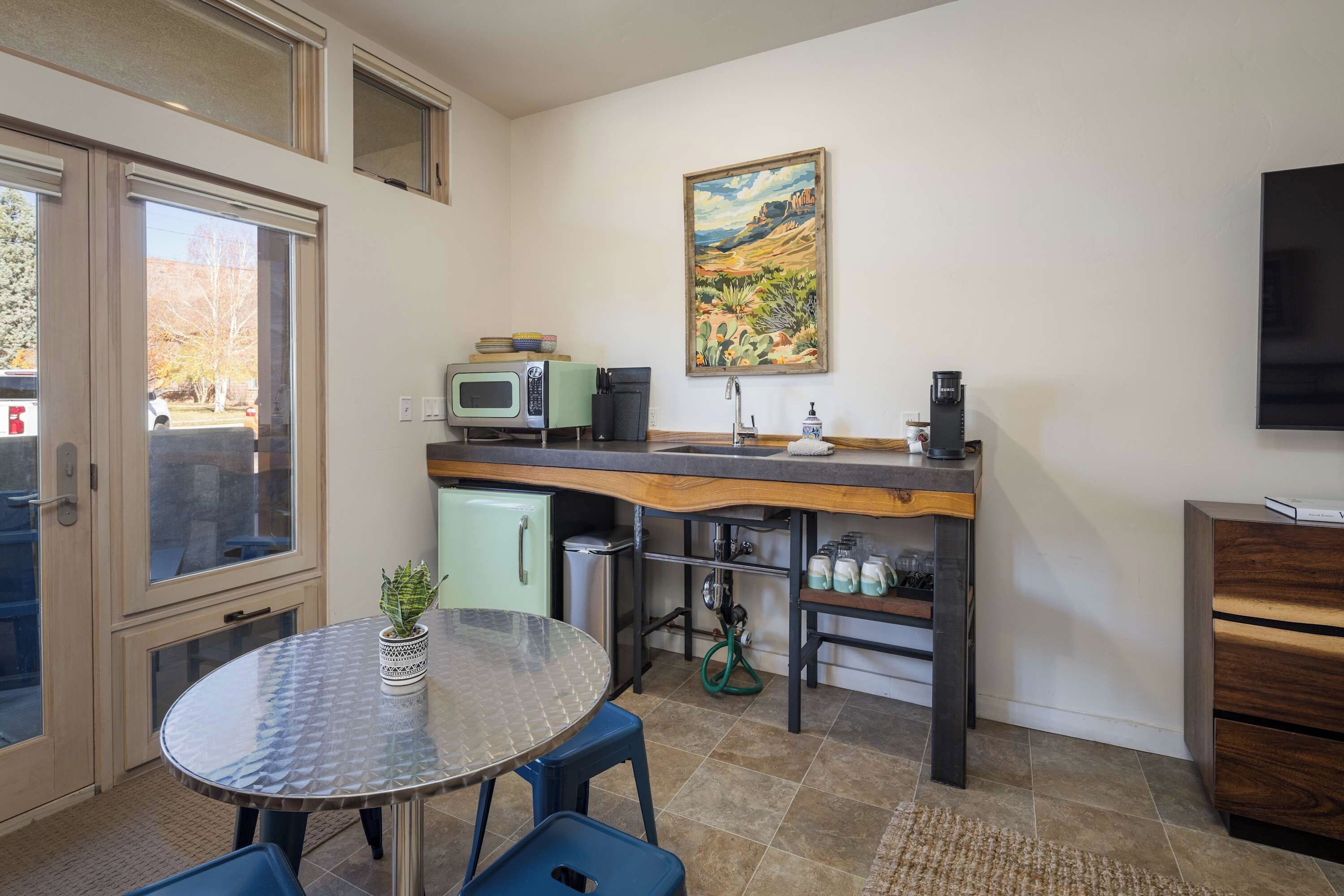 Cocina compacta con comedor, microondas, cafetera y un cuadro en la pared.