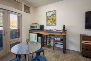 A compact kitchen with a dining area, a microwave, a coffee maker, and a painting on the wall.