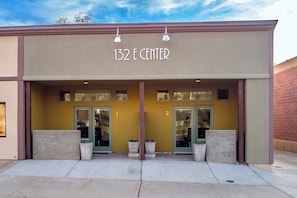 A building with the sign "132 E CENTER" above the entrance. There are two doors, each with a window above. The building has a beige facade with a brown trim.
