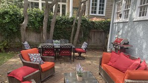 Un espacio al aire libre con patio, mobiliario de mimbre, una mesa de centro de vidrio y una parrilla.