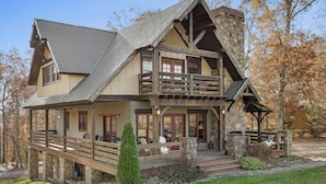 A large, multi-story log cabin with a stone foundation, wooden balconies, and a covered porch area.