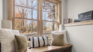 A cozy room with a large window, a bench with cushions, and a shelf with books and a decorative box.