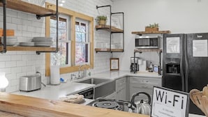 A modern kitchen with white brick walls, wooden shelves, a built-in microwave, a refrigerator, and a kettle.