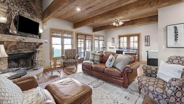 A spacious living room with a stone fireplace, leather furniture, and large windows.