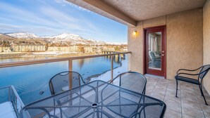 A balcony with a table and chairs, overlooking a river and mountains.