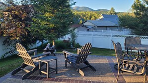 Um pátio com cadeiras Adirondack e uma mesa, cercado por um muro branco e um jardim.