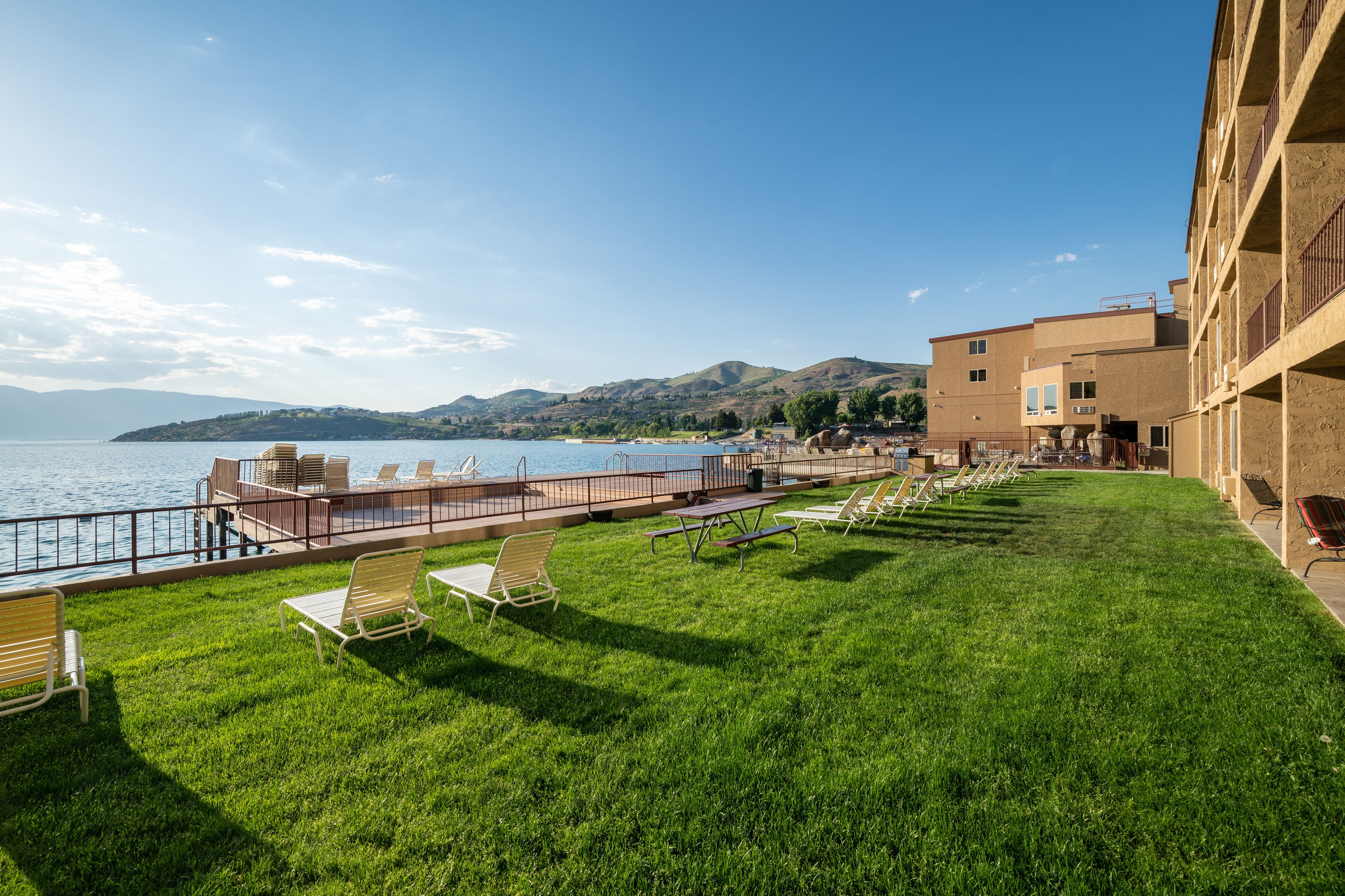 A grassy outdoor area with lounge chairs and a poolside area overlooking a body of water and hills.