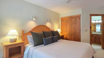 Un dormitorio con una cama grande, cabecera de madera, dos mesitas de noche con lámparas, un ventilador de techo y un armario.