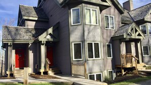 A multi-story residential building with a prominent red door, multiple windows, and a wooden deck. - Spacious ski-in, ski-out 2-BR Jay Peak Village Condo, right on trail. A/C incl.! (Jay)