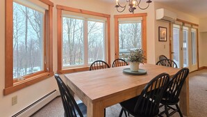 A dining area with a wooden table and chairs, large windows, and a chandelier. - Spacious ski-in, ski-out 2-BR Jay Peak Village Condo, right on trail. A/C incl.! (Jay)