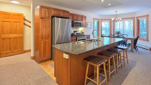 A modern kitchen with wooden cabinets, stainless steel appliances, and a large island with bar stools. - Spacious ski-in, ski-out 2-BR Jay Peak Village Condo, right on trail. A/C incl.! (Jay)