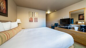 Une chambre d’hôtel avec un grand lit, une télévision, un bureau avec une machine à café et des œuvres d’art accrochées aux murs.