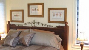 Una cama bien hecha con una colcha y almohadas a rayas, un cabecero de madera y una obra de arte con hojas enmarcada en la pared.