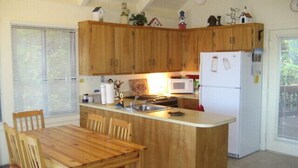 Una cocina con armarios de madera, un refrigerador blanco, un microondas, un lavamanos y una mesa de comedor con sillas.