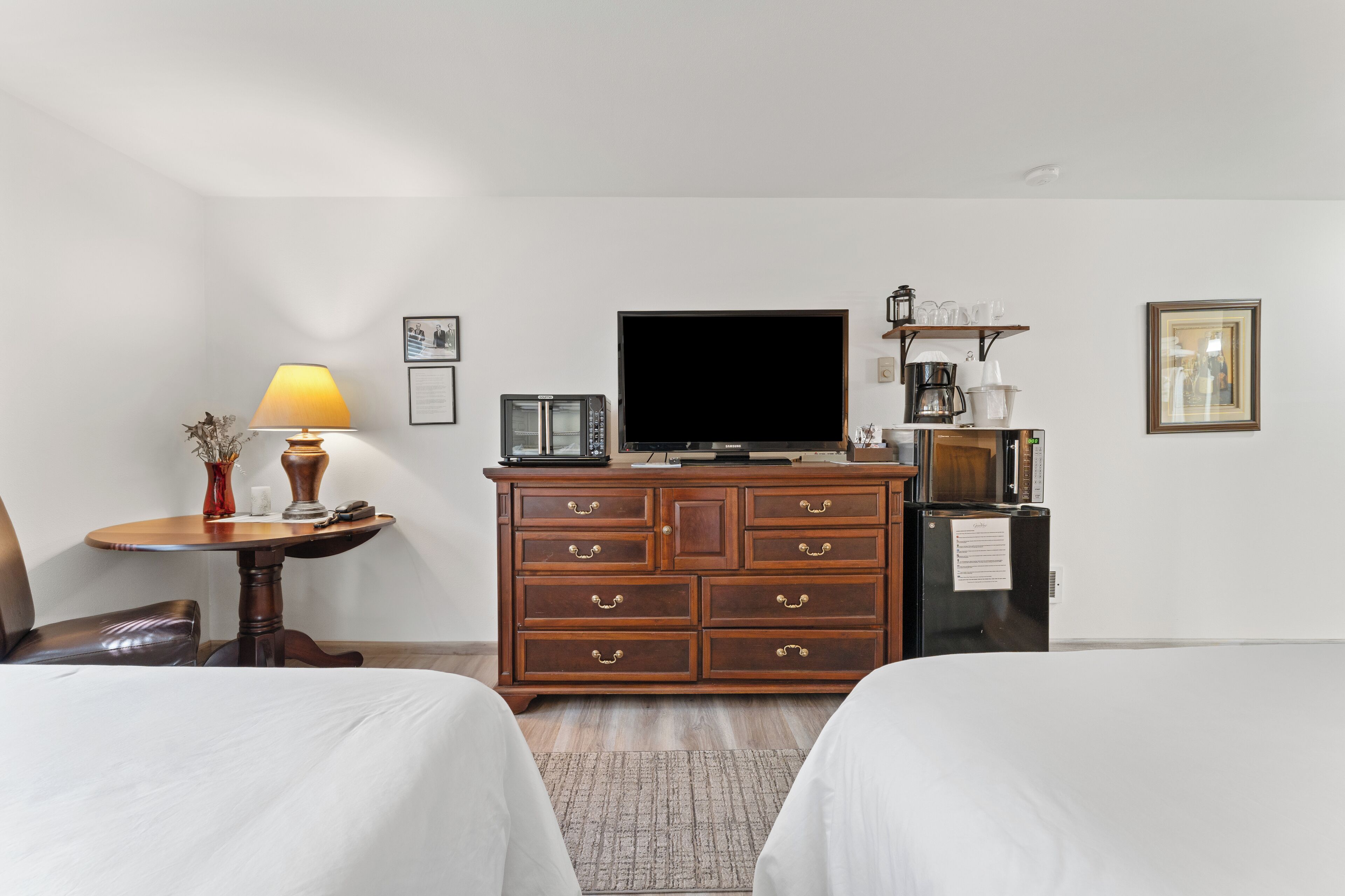 A hotel room with two beds, a wooden dresser, a television, a coffee maker, and a small table with a lamp.
