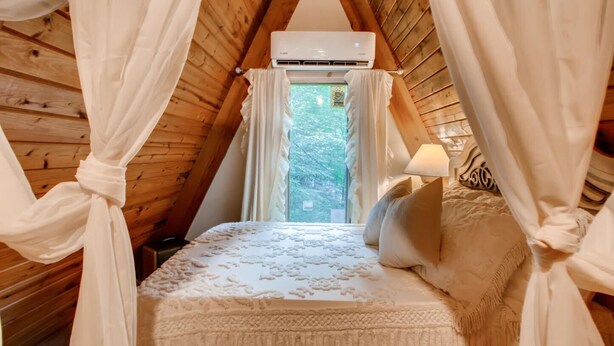 Ein gemütliches Schlafzimmer mit Holzbalkendecke, einem Himmelbett und einer Klimaanlage über dem Fenster.