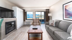Una sala de estar moderna con chimenea, un sofá, un sillón a rayas y vistas a las montañas a través de amplios ventanales.