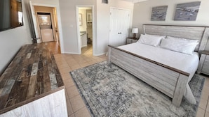 A bedroom with a wooden bed, a ceiling fan, a rug, and a view of the bathroom. - Duplex- What if I told you…You CAN afford Paradise! Make the Call today! 🤙 (Gulf Shores)