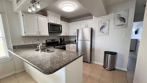 A kitchen with white cabinets, a granite countertop, stainless steel appliances, and a trash can. - Duplex- What if I told you…You CAN afford Paradise! Make the Call today! 🤙 (Gulf Shores)