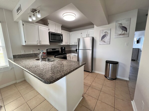 A kitchen with white cabinets, a granite countertop, stainless steel appliances, and a trash can. - Duplex- What if I told you…You CAN afford Paradise! Make the Call today! 🤙 (Gulf Shores)