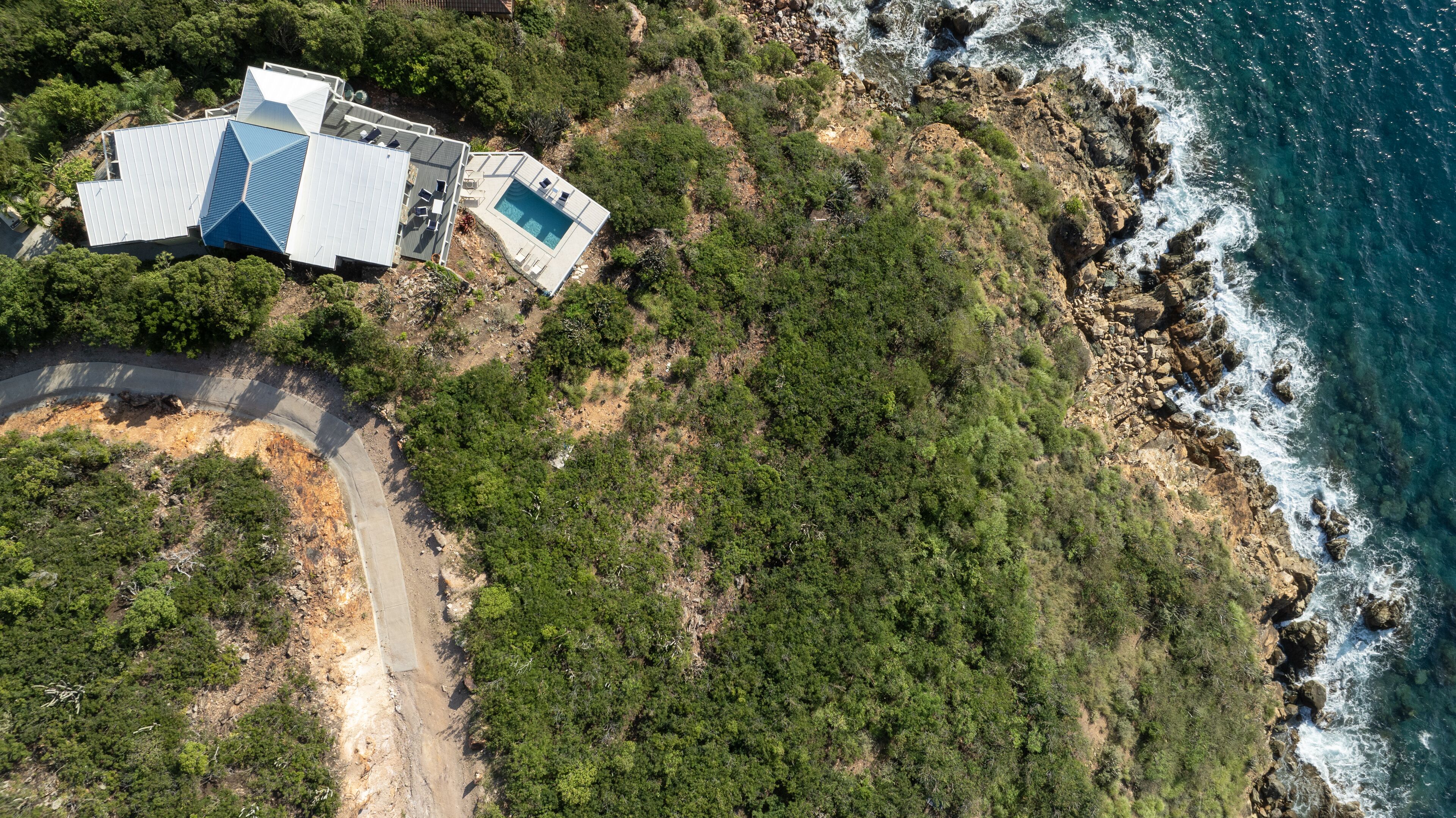Vue aérienne d’une propriété située sur la côte, avec une piscine, une route et une végétation luxuriante.