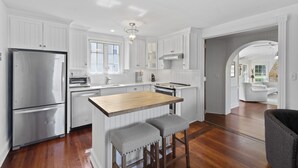 A modern kitchen with white cabinetry, stainless steel appliances, and a wooden island with bar stools. - Water front home on the Cohansey River (Bridgeton)