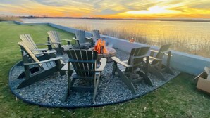 A circular outdoor seating area with Adirondack chairs around a fire pit, overlooking a body of water during sunset. - Water front home on the Cohansey River (Bridgeton)