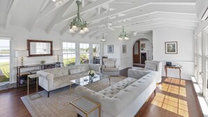 A spacious living room with a large sectional sofa, a glass coffee table, and a fireplace. There are multiple windows providing natural light and a view of the outdoors. - Water front home on the Cohansey River (Bridgeton)