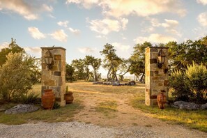 Un arco de piedra rústico con faroles, rodeado de follaje y un camino de grava.