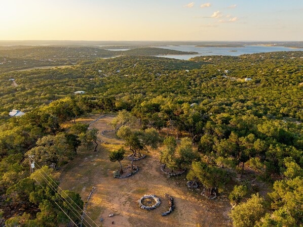 A forested area with a circular stone structure, a clear sky, and a distant body of water.
