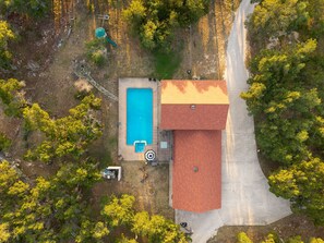 Una vista aerea di una proprietà con piscina, portico coperto e un edificio con tetto rosso.