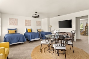 A bedroom with two beds, a dining table with chairs, a TV, and decorative wall art.