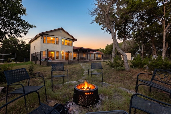 A two-story house with a fire pit in the backyard, surrounded by outdoor furniture.