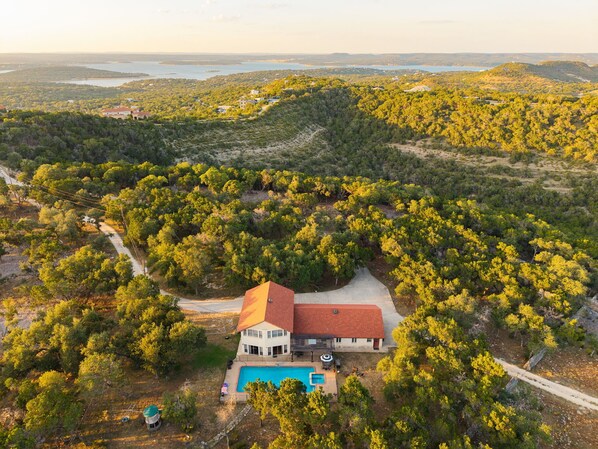 Una casa grande con piscina, rodeada de árboles frondosos.