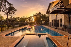 Una piscina con vistas a la puesta de sol, rodeada de árboles y un edificio de fachada de piedra.