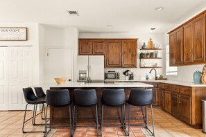 Cocina con una isla central, taburetes de bar, armarios de madera y una puerta blanca.