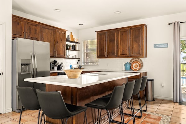 A modern kitchen with a central island, bar stools, a refrigerator, and wooden cabinets.
