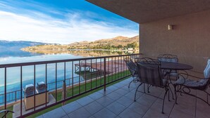 Un balcón con vistas a un lago y montañas, mobiliario exterior y una parrilla.