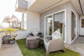 Relax in a serene outdoor space with a curved sofa and woven side table, surrounded by lush greenery and a seamless indoor-outdoor connection.