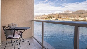 Varanda com mesa e cadeiras, com vista para um corpo de água e uma cidade distante com montanhas.