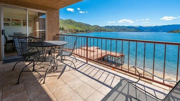 Un balcone con tavolo e sedie, affacciato su un lago con montagne sullo sfondo.