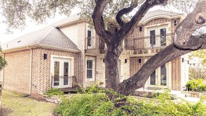 A two-story brick house with a large tree in front, a balcony, and a well-maintained garden. - Huge Home in Downtown ATX/Large Groups Welcome/Walk Everywhere!!! (Austin)