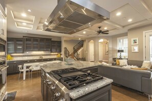 A spacious kitchen with dark cabinets, a large island, a gas stove, and a ceiling fan. - Huge Home in Downtown ATX/Large Groups Welcome/Walk Everywhere!!! (Austin)